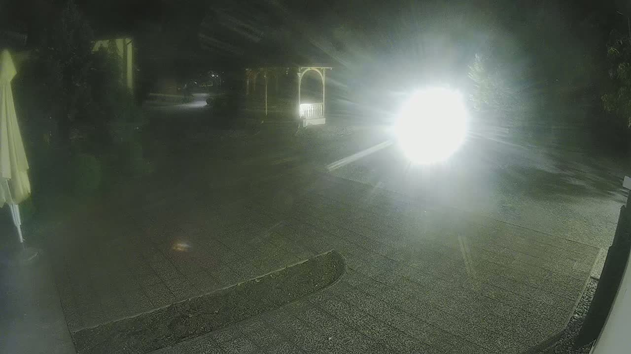 A nighttime view of a gravel driveway leading to a gazebo, illuminated by a bright light source.