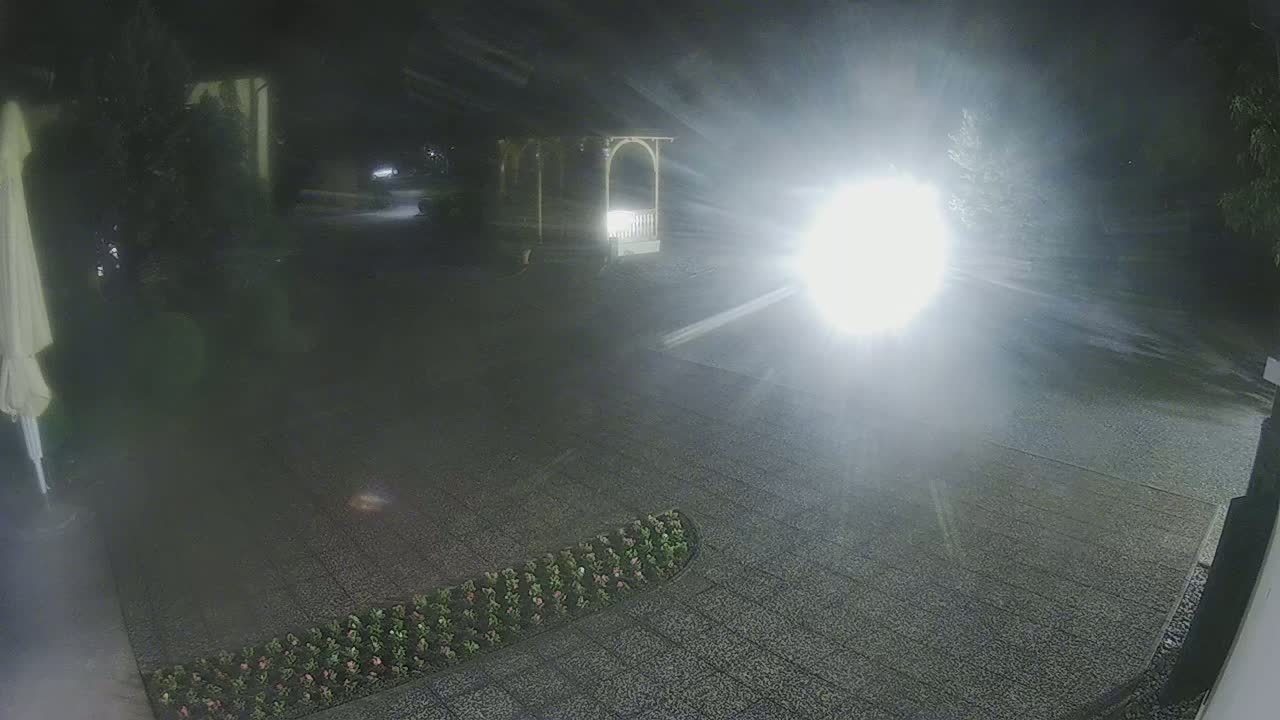 A nighttime view of a paved area with a gazebo and a strip of low landscaping, illuminated by a bright light source.