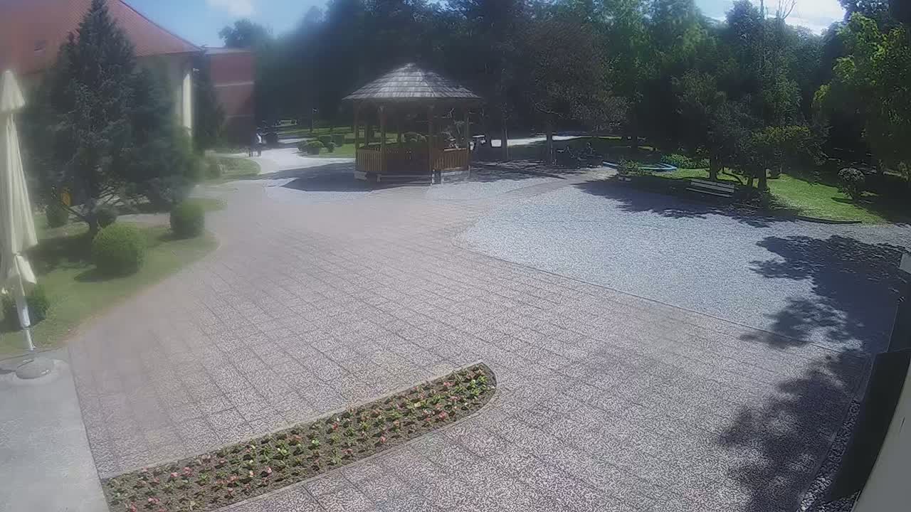 A paved courtyard with a gazebo, landscaping, and surrounding trees on a sunny day.