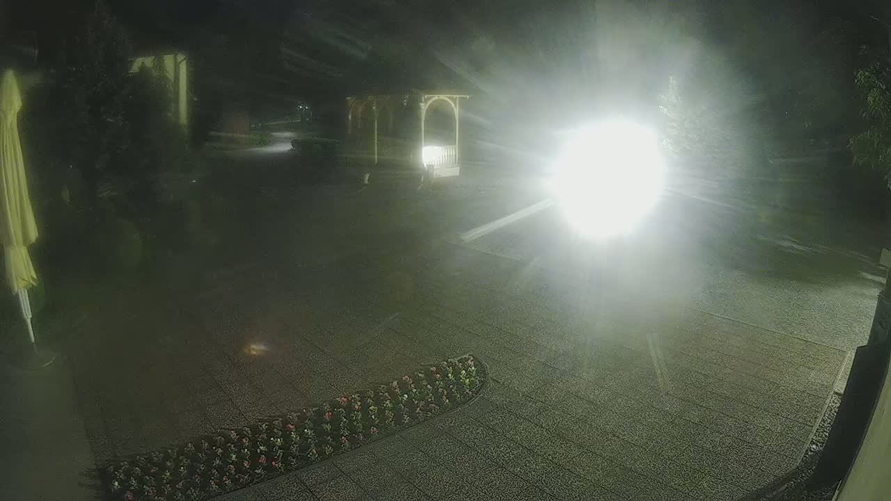 A nighttime scene of a paved area with a gazebo and flower bed, illuminated by a bright light source.