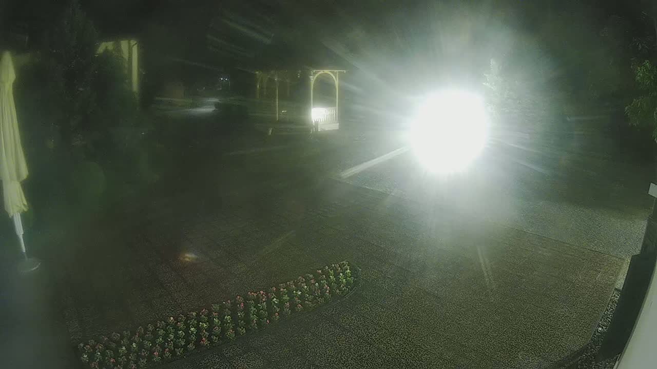 A nighttime view of a gravel area with a gazebo and flower bed, illuminated by a bright light source.