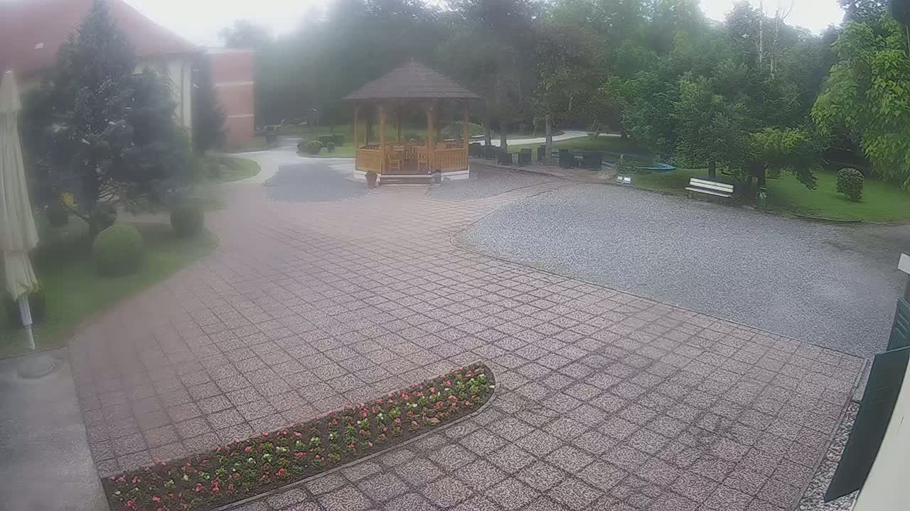 A paved courtyard with a wooden gazebo and a flower bed is partially obscured by a hazy atmosphere.