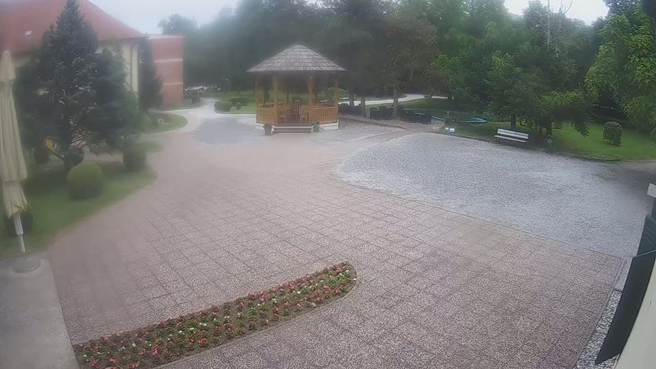 A paved courtyard with a wooden gazebo, surrounded by landscaping, on an overcast day.