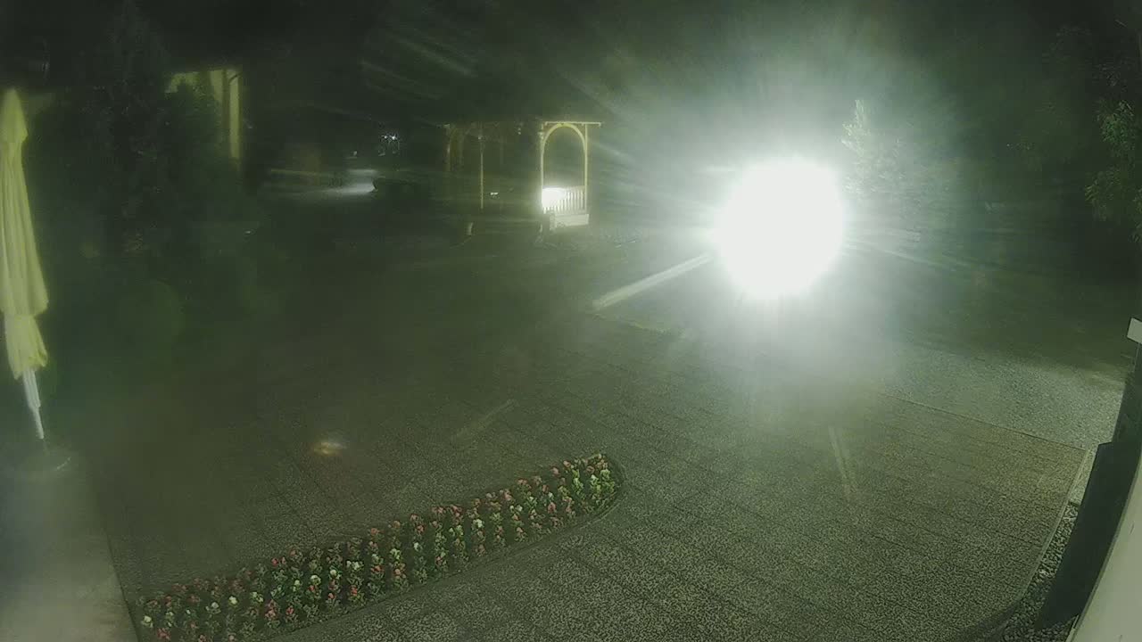 A nighttime outdoor scene shows a gravel area with a flower bed, a gazebo, and bright light sources that obscure much of the view.