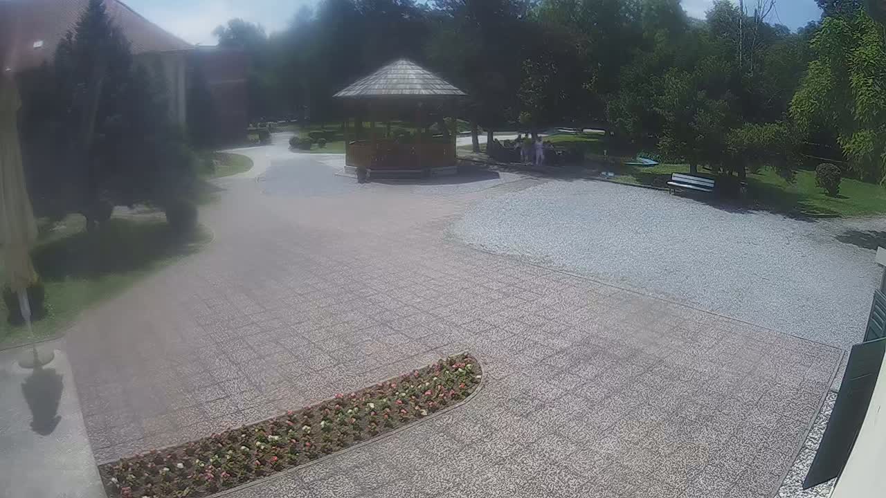A gravel courtyard with a gazebo, a few people, some landscaping, and a building in the background on a partly sunny day.
