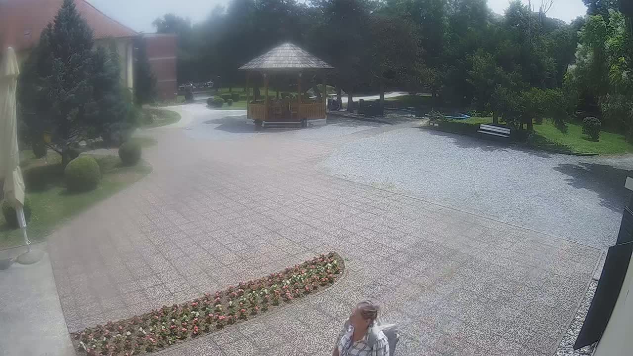 A paved courtyard with a gazebo, landscaping, and a person, all under a sunny sky.