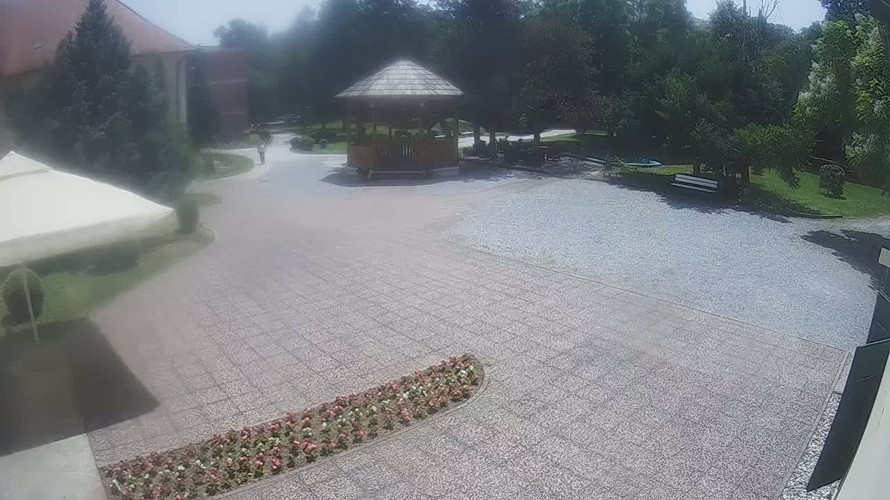 A gravel courtyard with a gazebo, flowerbeds, and a section of building is visible under sunny skies.