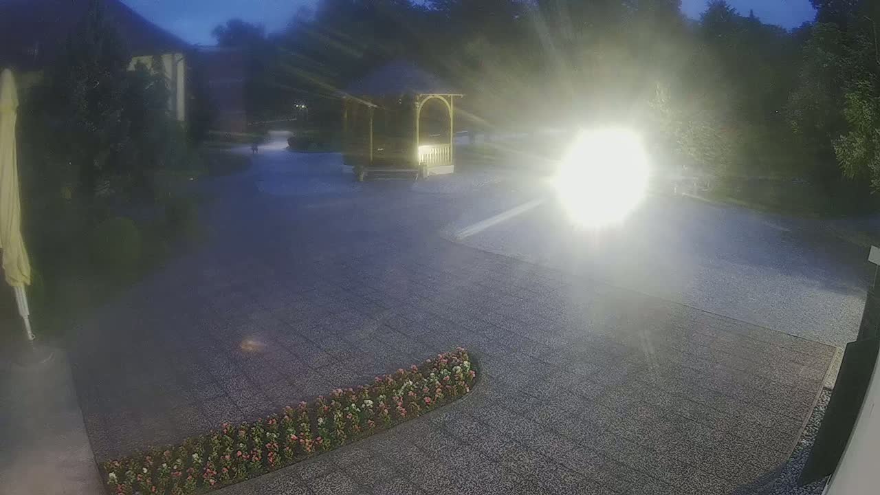 A paved area with a gazebo and flower bed is illuminated at night by a bright light source.