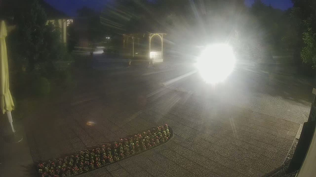 A nighttime, brightly lit paved area with a gazebo and flowerbeds, partially obscured by glare.