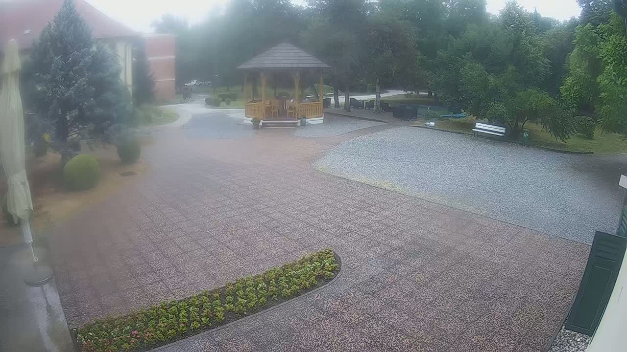 A gravel courtyard with a wooden gazebo and landscaping is seen on an overcast day.