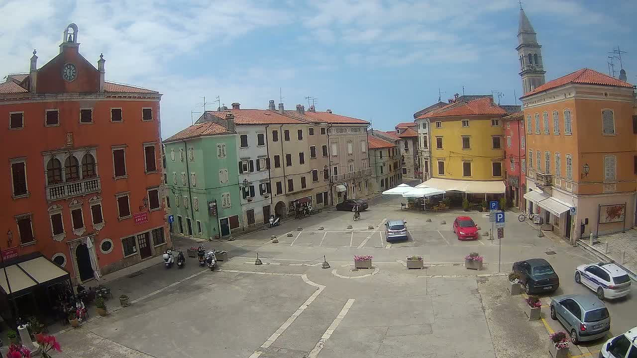 A mostly empty town square with colorful buildings surrounding it under a partly cloudy sky.