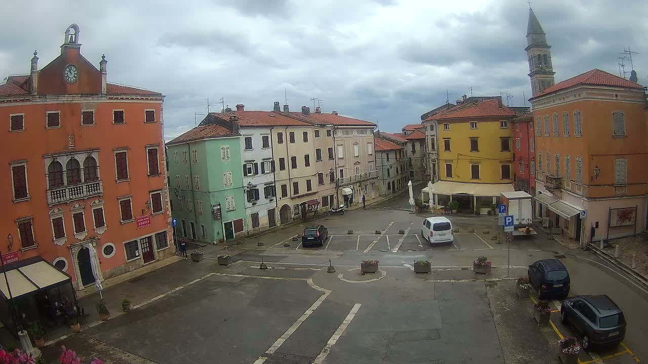 A town square with colorful buildings, a few parked cars, and overcast skies.