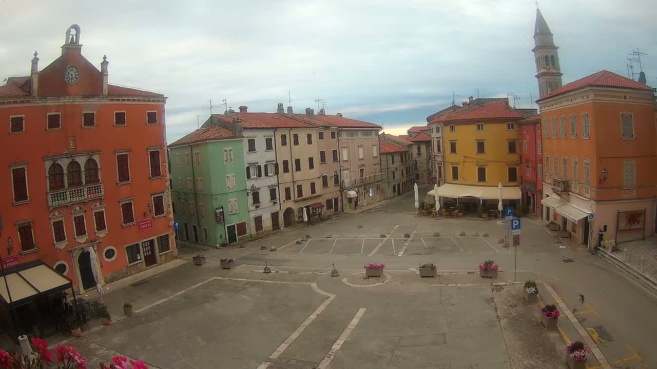 A mostly empty town square is surrounded by colorful, historic buildings under a cloudy sky.