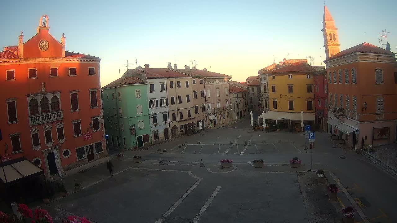 A mostly empty town square in the early morning, surrounded by colorful buildings, under a clear sky.