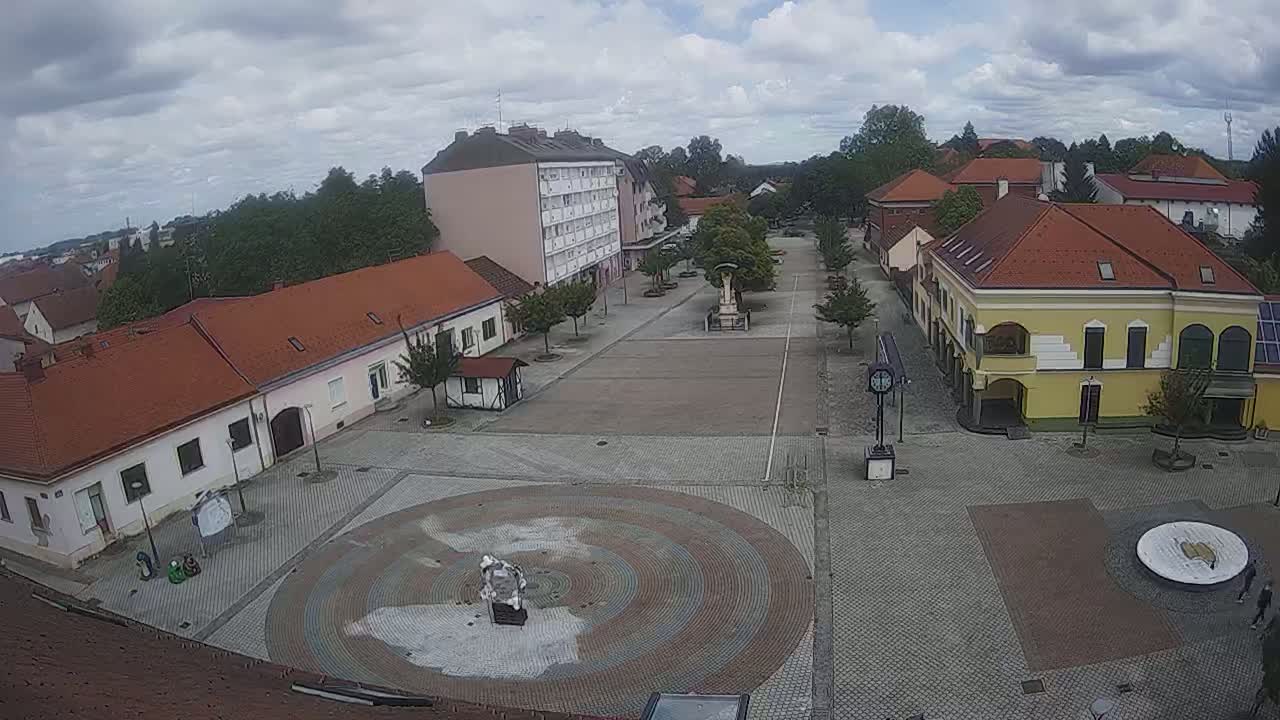 A town square with low buildings surrounding it, under a partly cloudy sky.