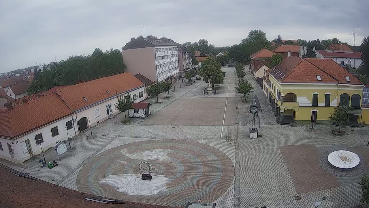 An overcast day reveals a town square with several low buildings, a large multi-story building, and a circular paved area in the center.