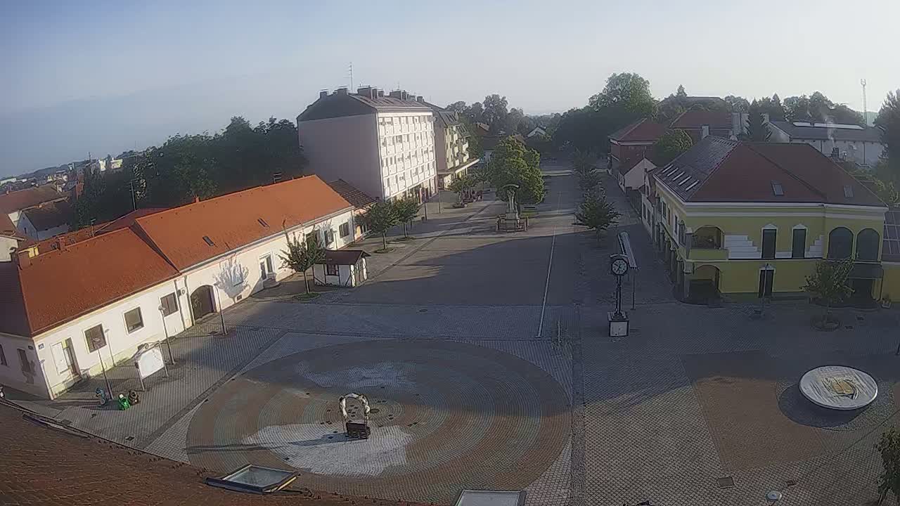 A mostly empty town square with several buildings surrounding it on a clear, sunny morning.