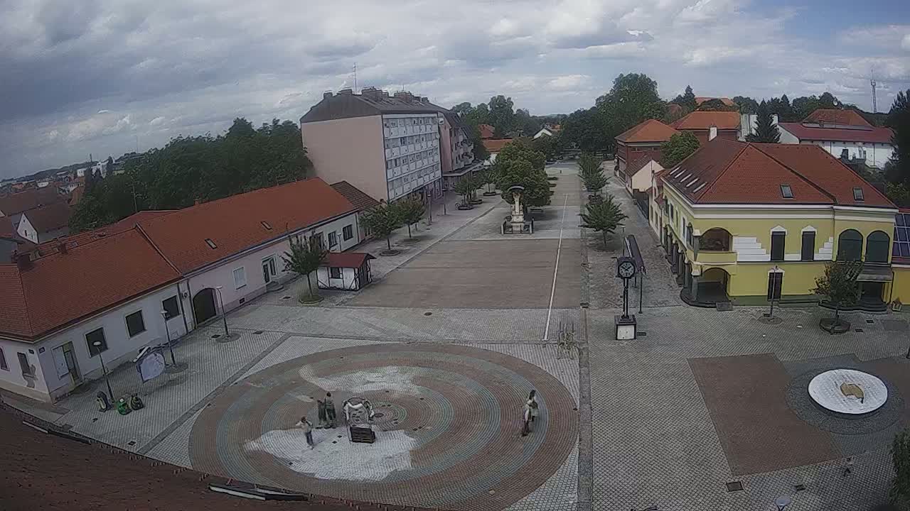 A town square with several low buildings and a large, circular paved area under a cloudy sky.