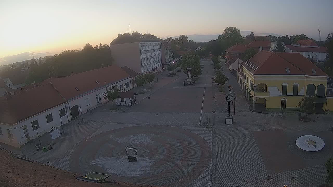 A town square with low-rise buildings is seen at sunrise under a clear sky.