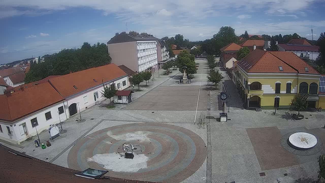 A town square with several low buildings and a circular paved area under a partly cloudy sky.