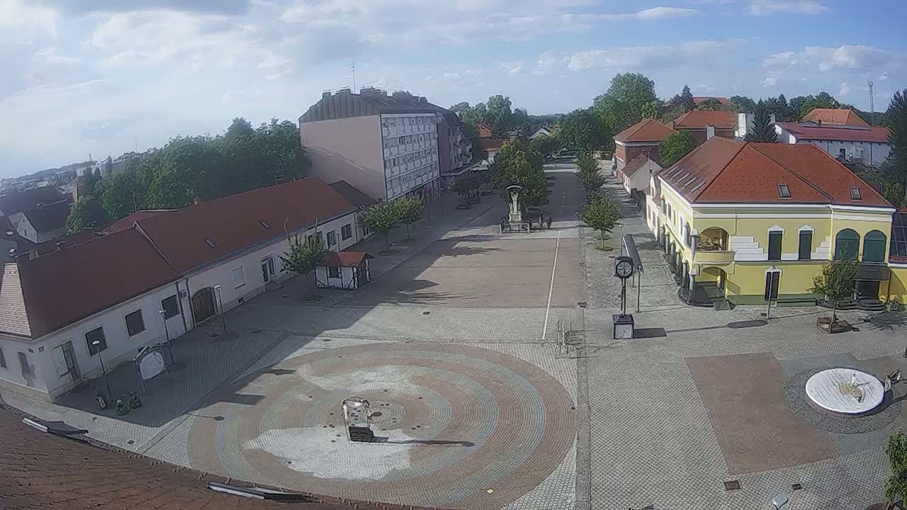 A mostly empty town square with low buildings surrounding it under a partly cloudy sky.