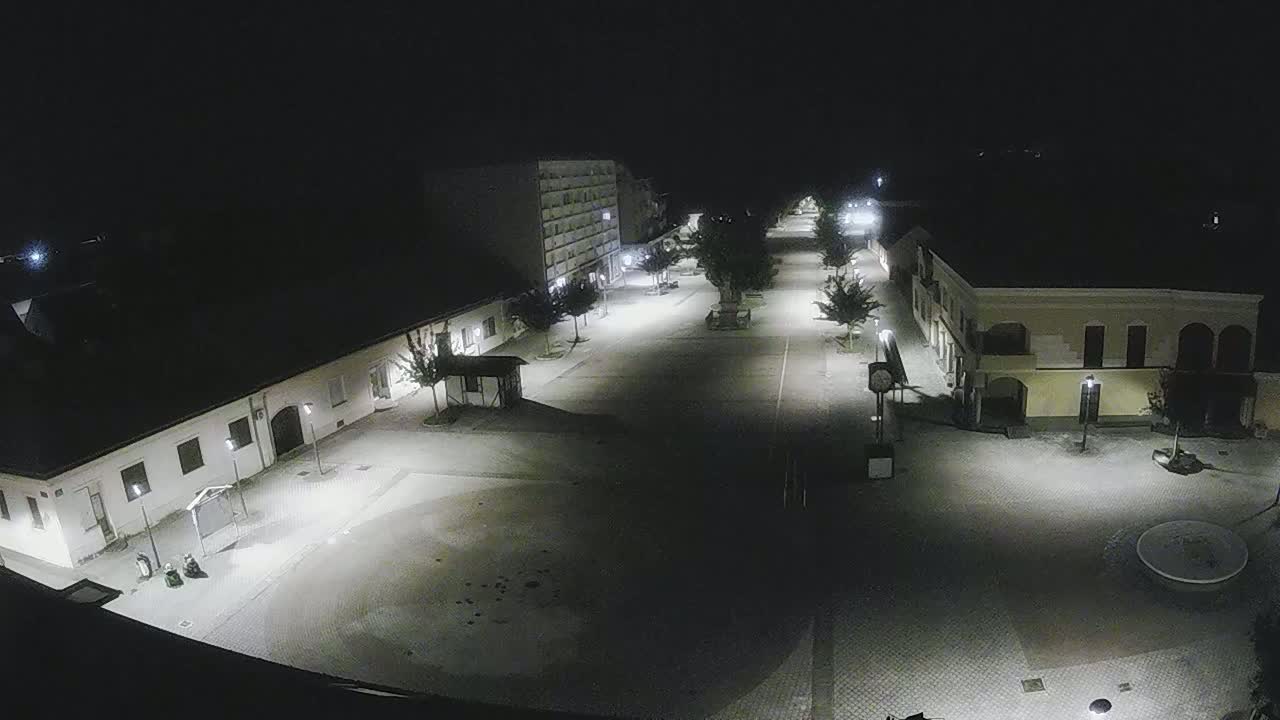 A mostly empty town square at night, illuminated by streetlights, is seen from an elevated vantage point.