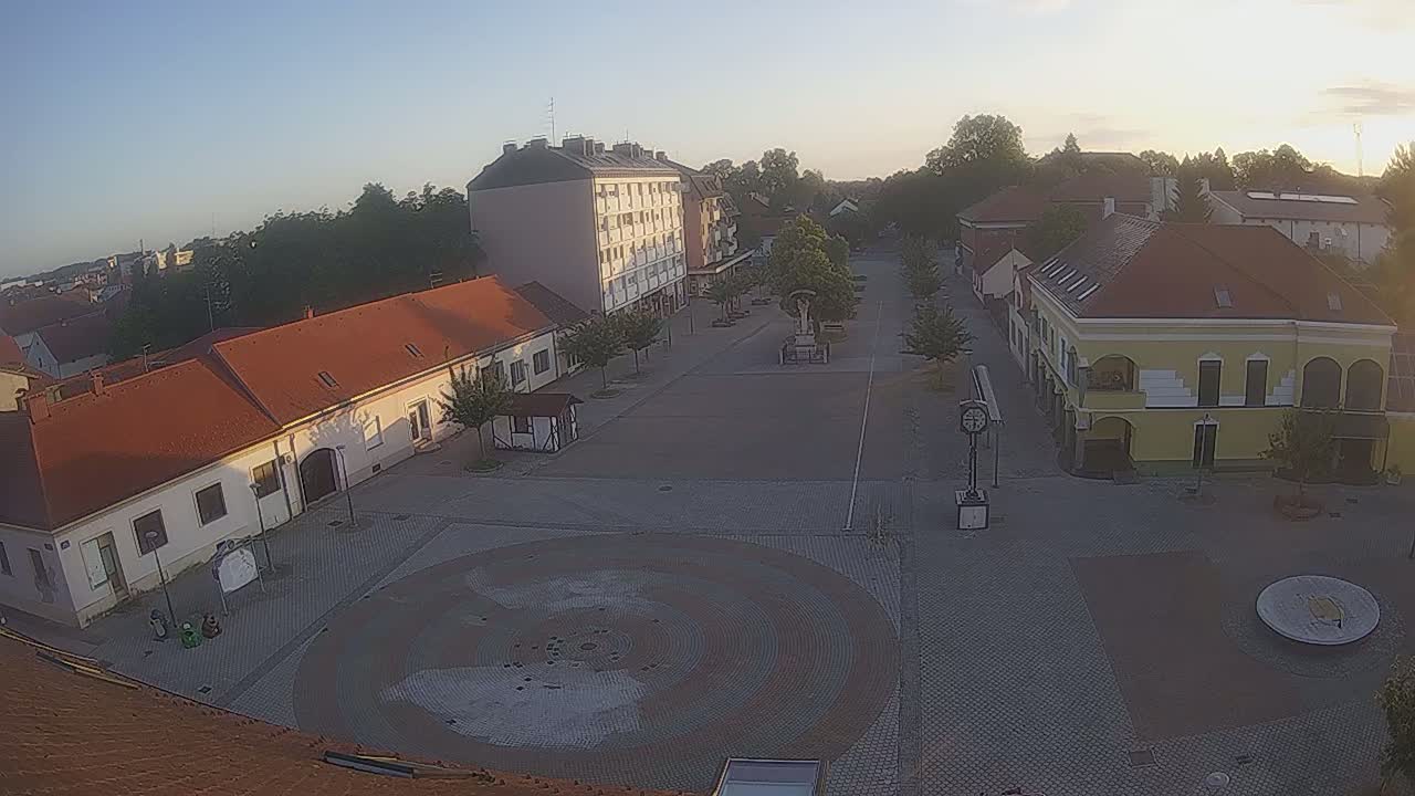 A mostly empty town square with buildings on all sides, under a clear, bright sky at sunrise.