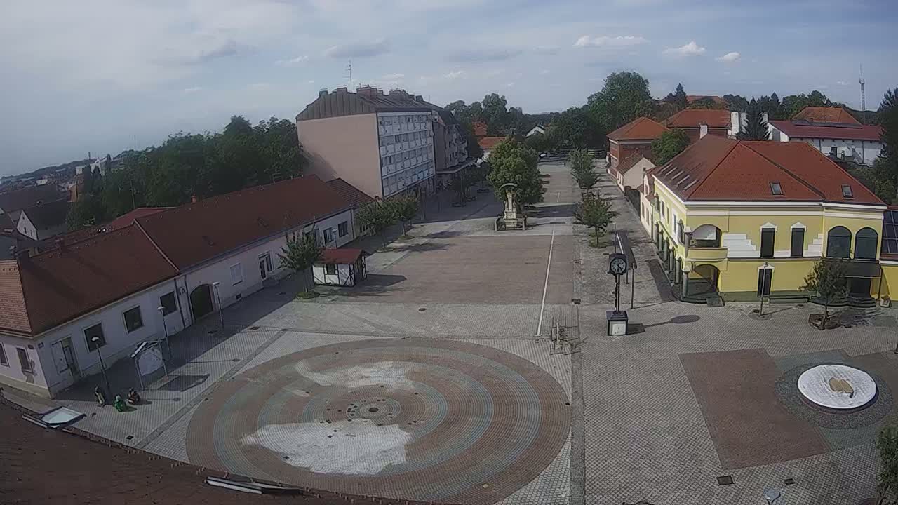 A mostly empty town square with several buildings surrounding it, under a partly cloudy sky.