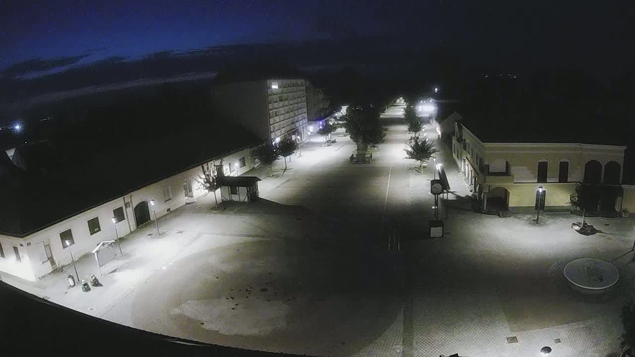 An empty town square at night, illuminated by streetlights under a dark, clear sky.