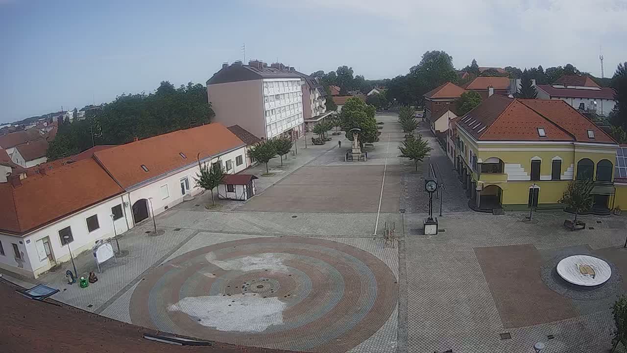 An empty town square with buildings surrounding it, under a mostly clear sky.