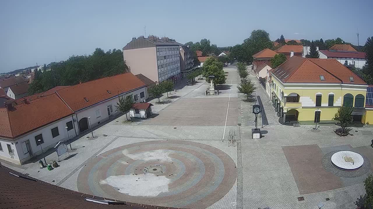 A town square with low buildings and a large circular paved area in the center, under sunny skies.