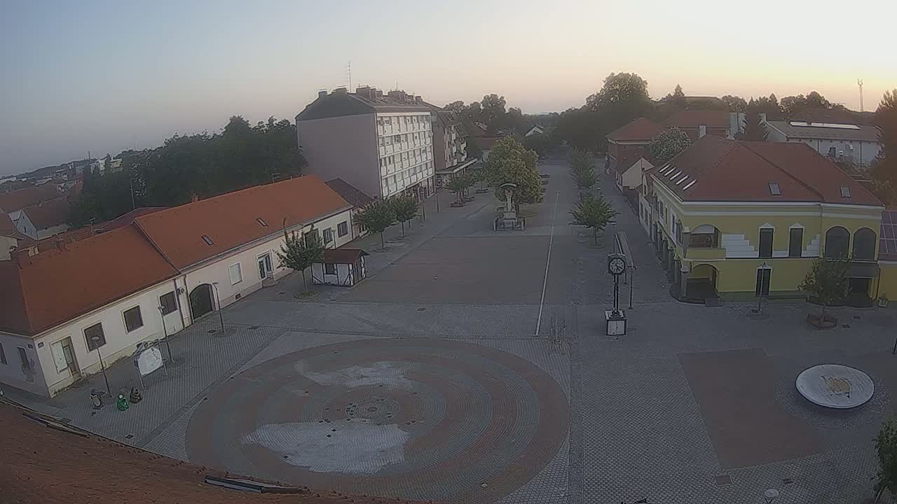 A mostly empty town square with several buildings surrounding it, under a clear sunny sky.