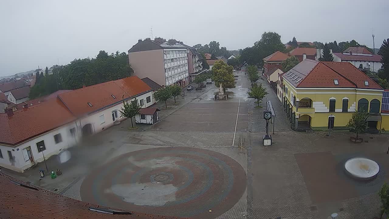 A town square with several buildings surrounding it, is seen on a rainy day.
