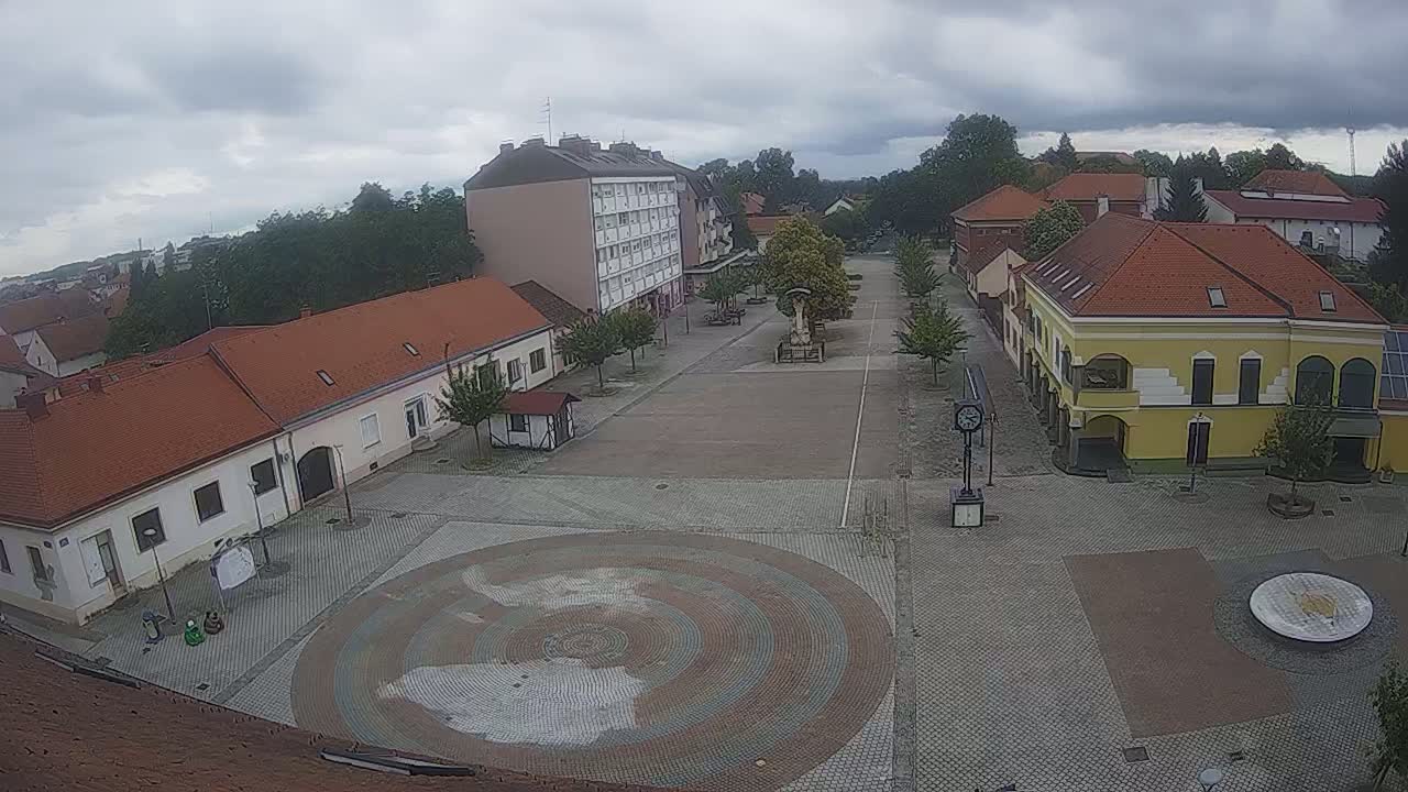 A town square with low buildings and a circular paved design in the center, under an overcast sky.
