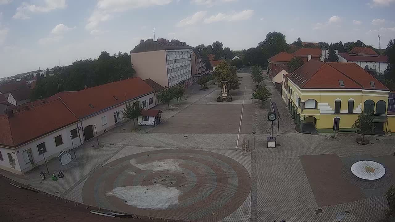 A town square with several low buildings and a large circular paved area is visible under partly cloudy skies.