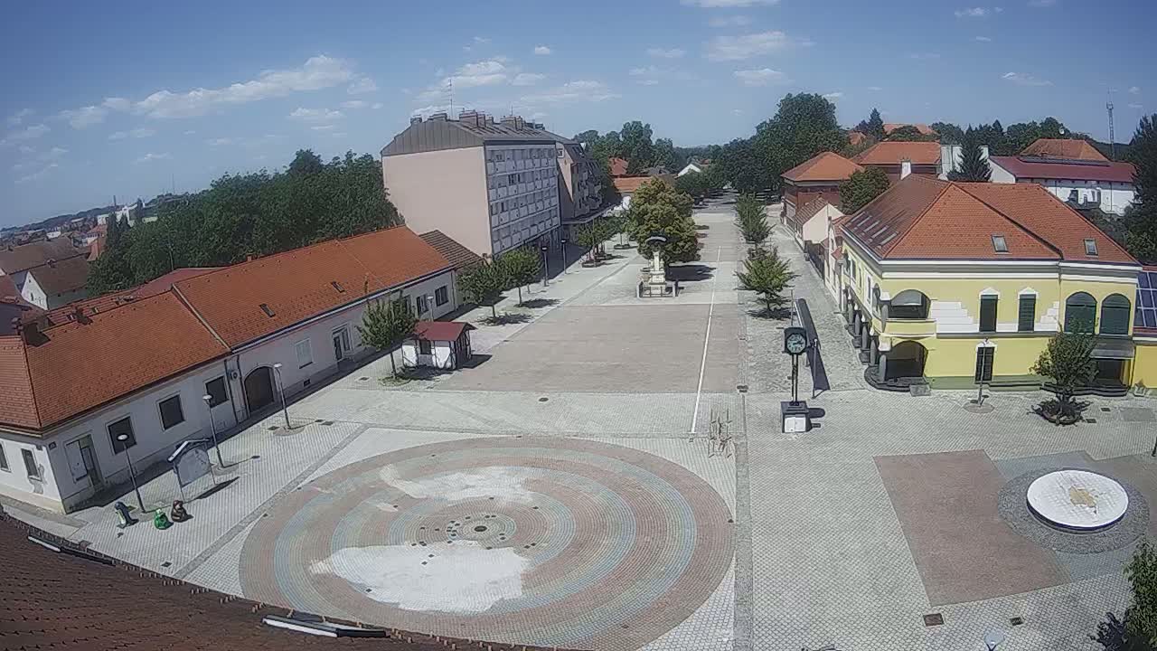 A town square with low buildings and a circular paved area is seen under a clear, sunny sky.