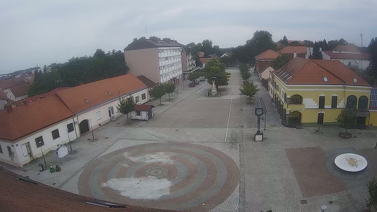 A town square with low buildings and a circular paved area in the center, under an overcast sky.