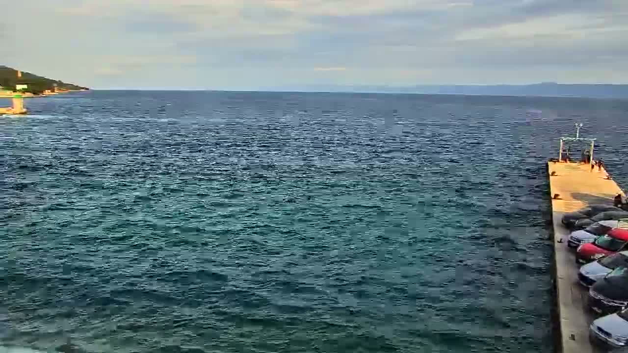 A long pier extends from a shoreline into a somewhat choppy sea under a partly cloudy sky.