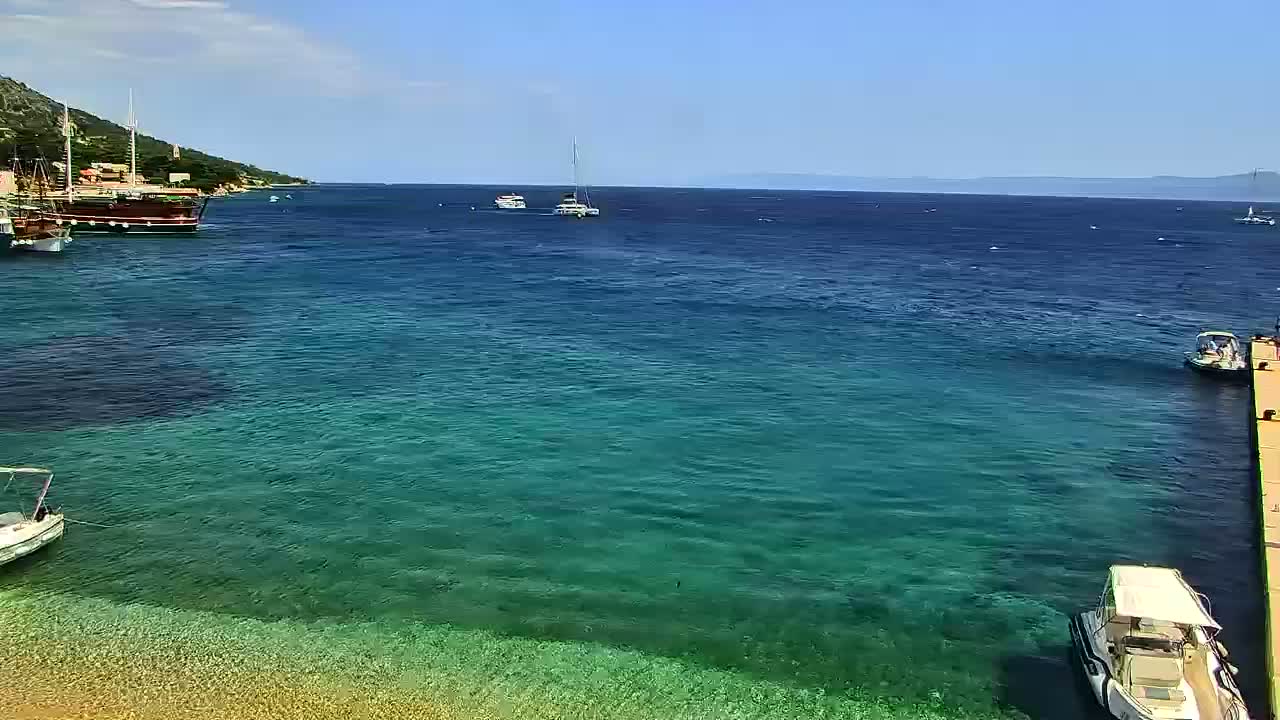 Several boats are moored in a calm, clear turquoise sea near a rocky shoreline under a sunny sky.
