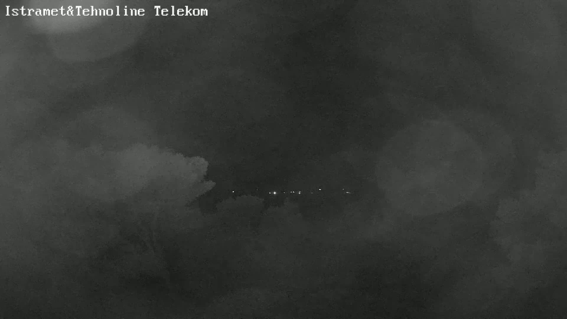 A nighttime, hazy, or foggy scene shows a distant line of faint lights.