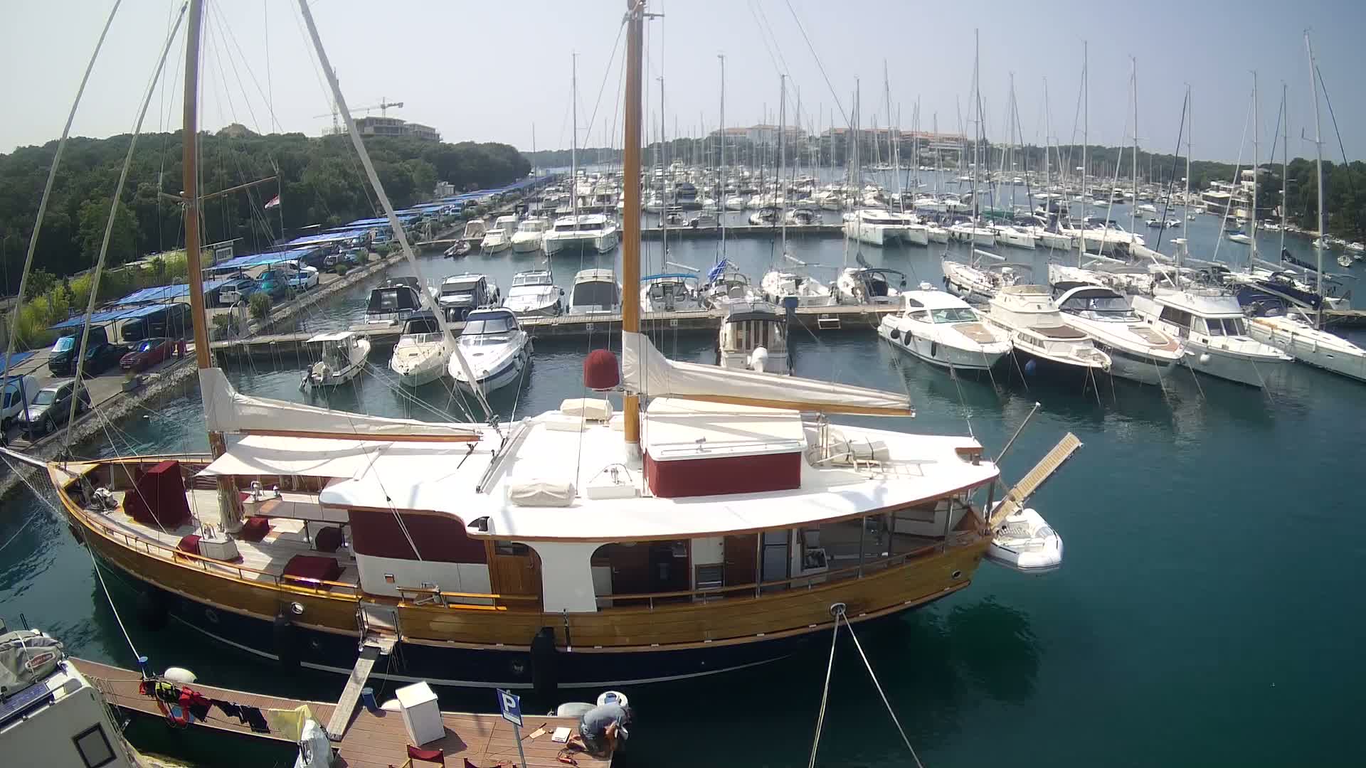 A large wooden sailboat is docked in a marina filled with many other boats on a sunny day.
