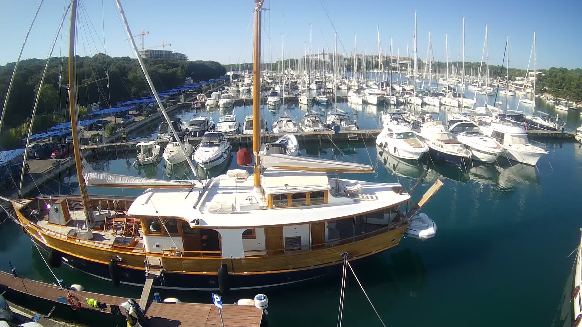 A large wooden sailboat is docked in a marina filled with many other boats on a sunny day.