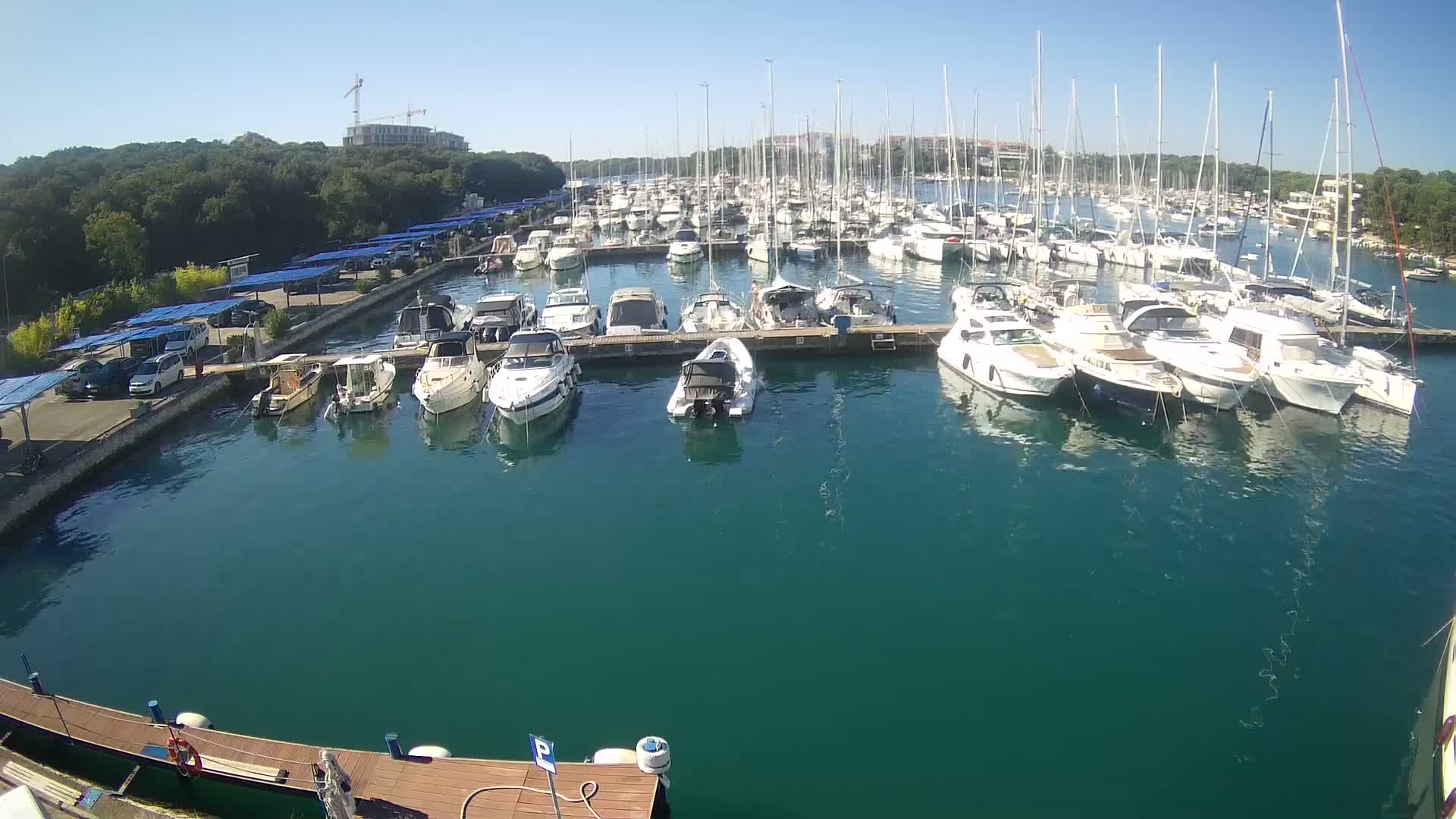 A marina filled with numerous sailboats and motorboats is shown on a sunny day with clear skies.