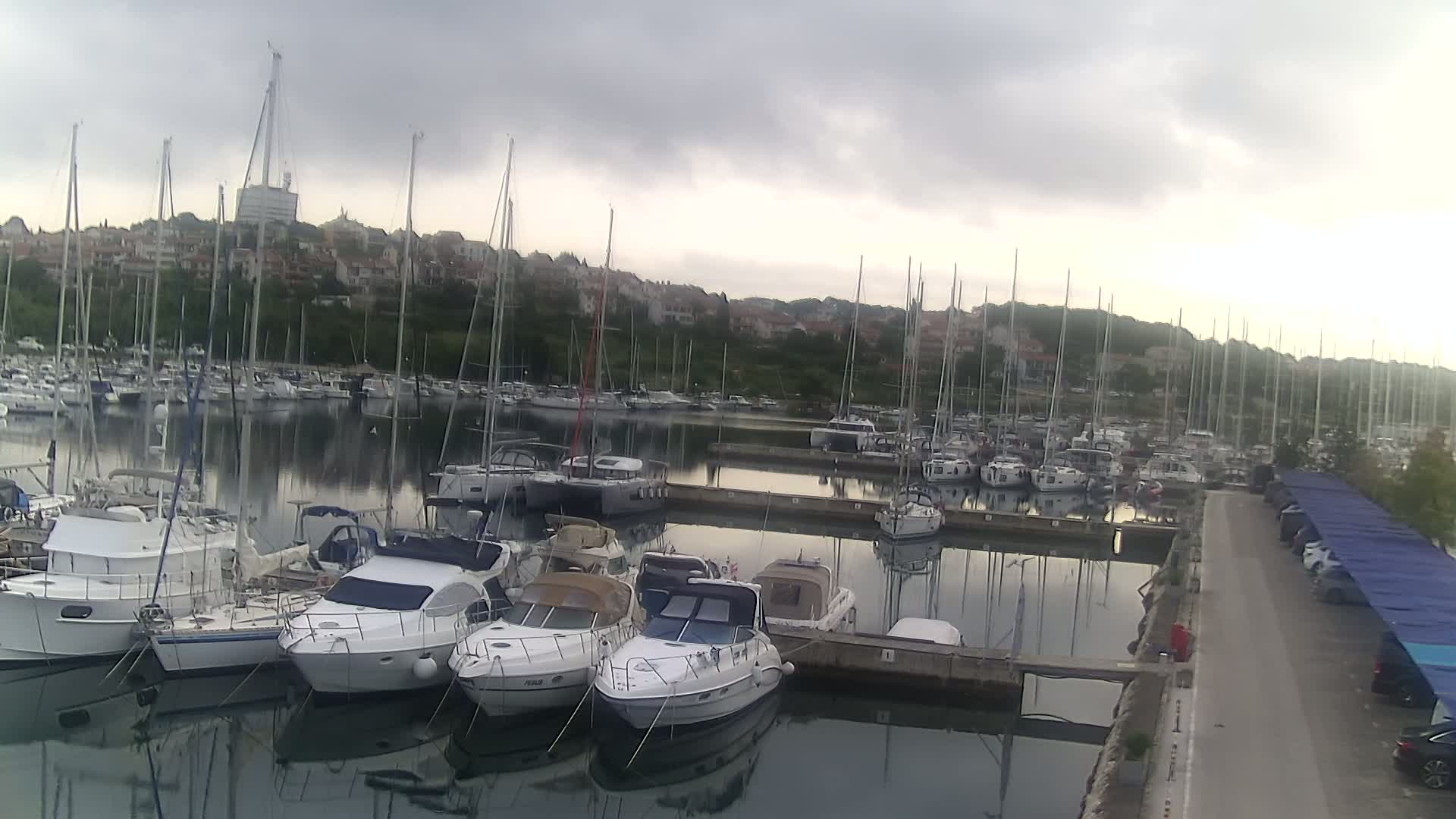 Many sailboats and motorboats are docked in a marina on a cloudy day.