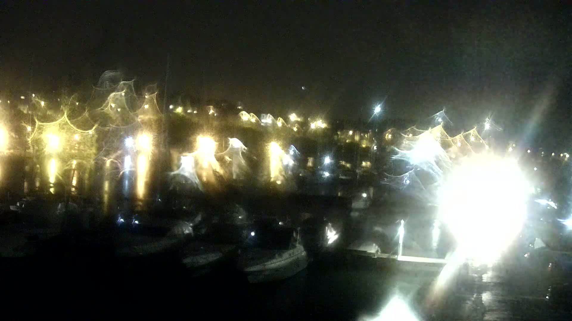 A rain-streaked nighttime view of a harbor filled with boats and illuminated by many lights.