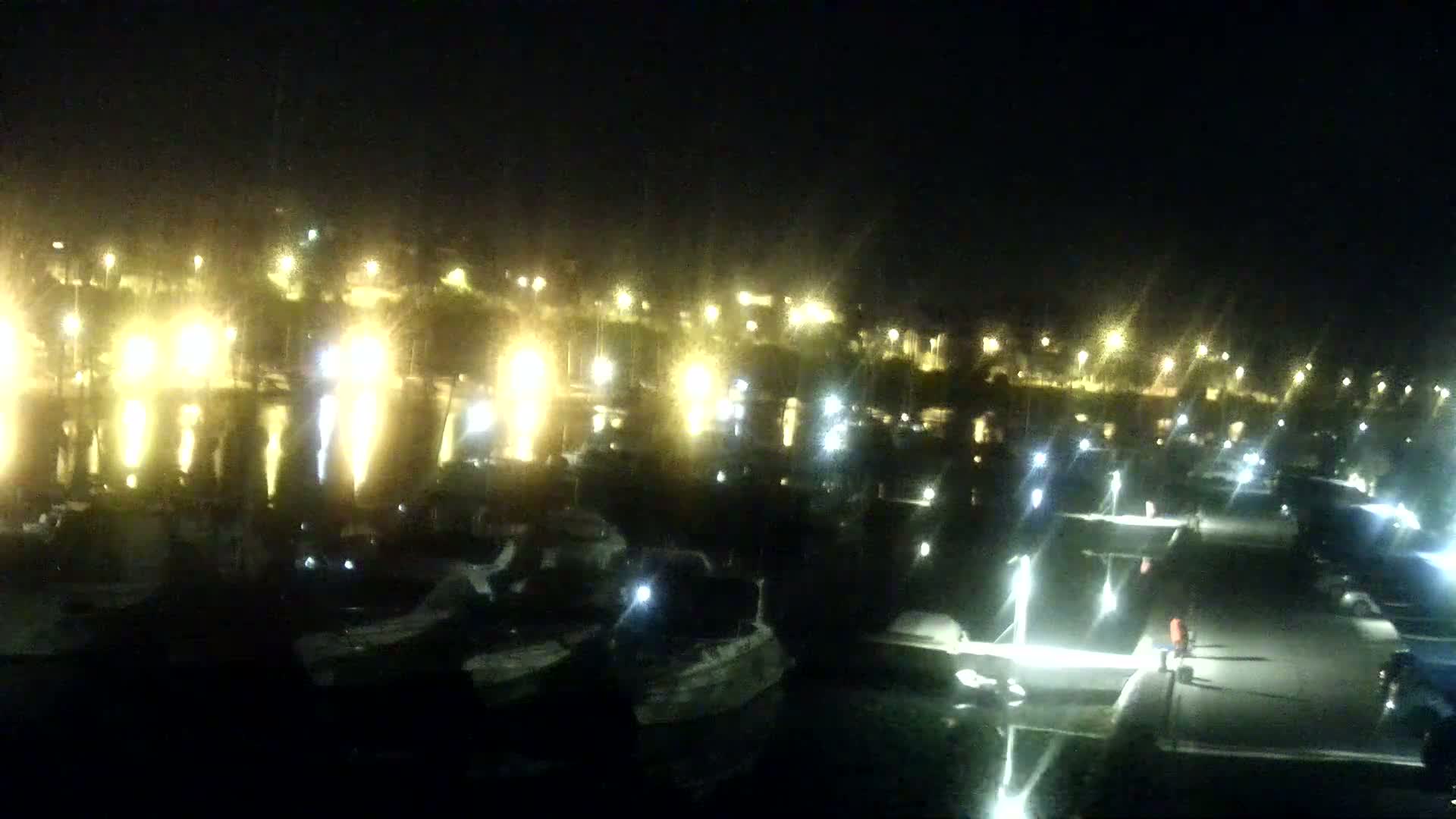Many boats are docked at a marina at night, illuminated by numerous lights.
