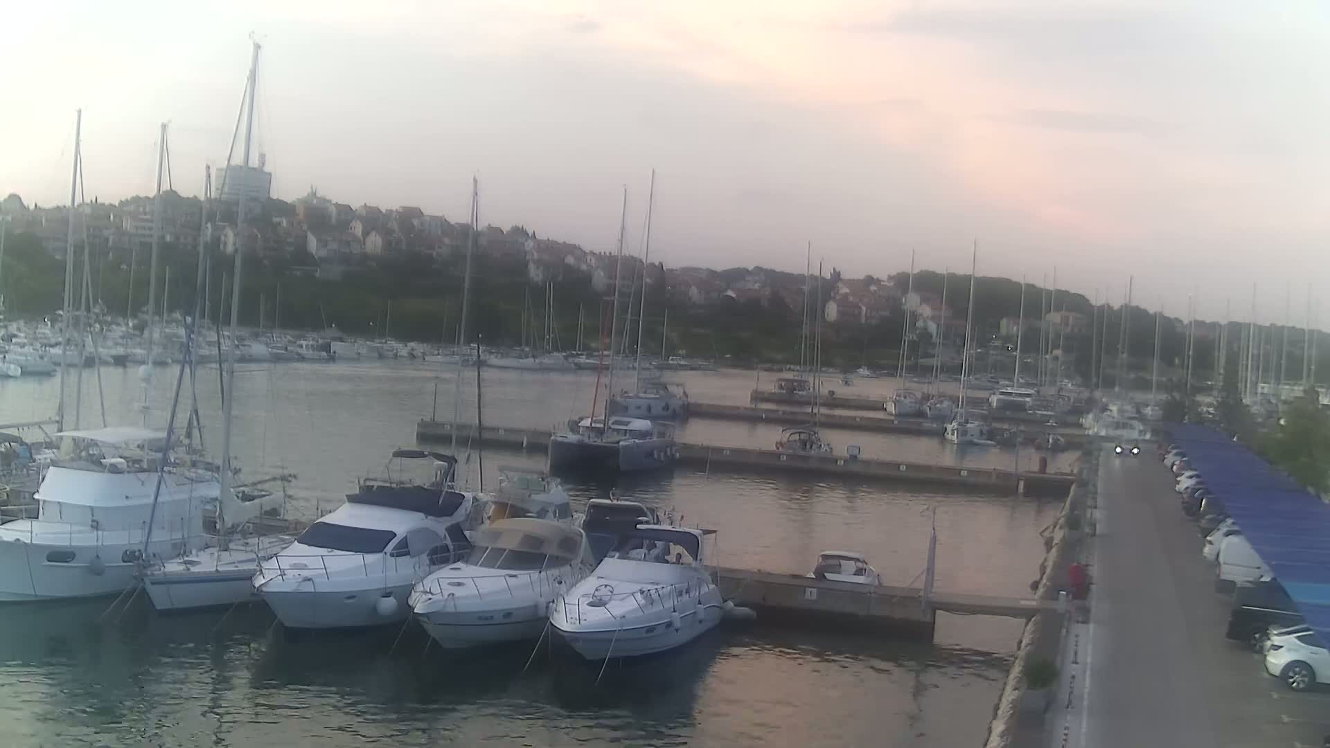 A marina filled with sailboats and motorboats is shown on a calm, overcast evening.