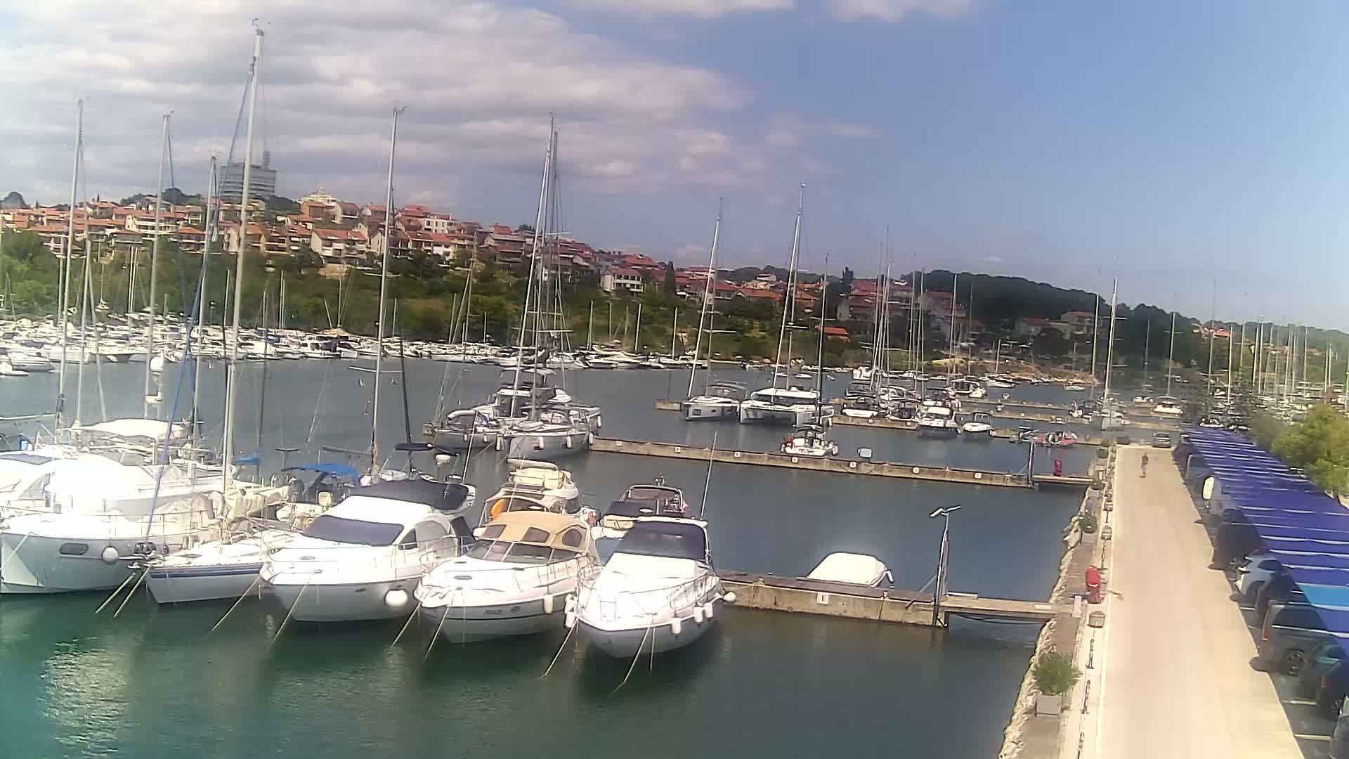A marina filled with numerous sailboats and motorboats under a partly cloudy sky.