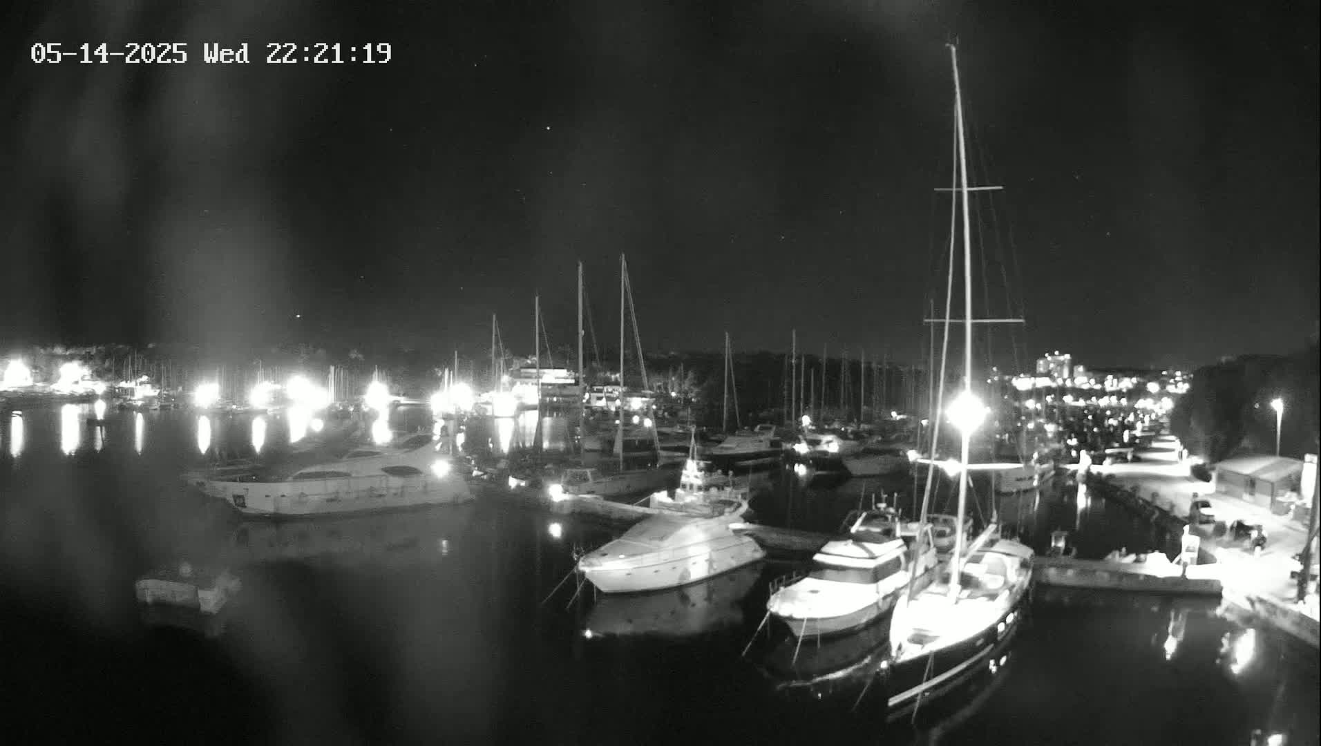 A nighttime, low-light view of a marina filled with sailboats and motor yachts, illuminated by dock lights.