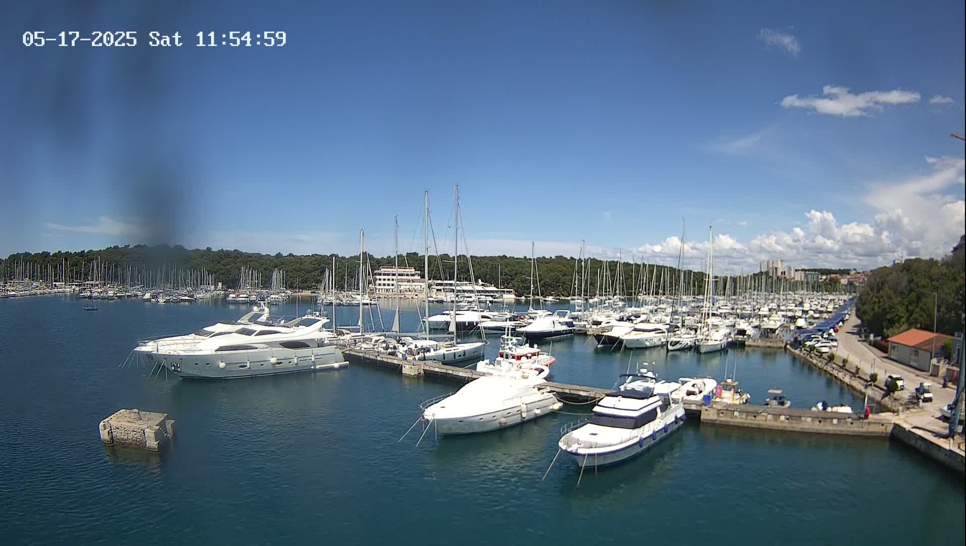 A marina filled with numerous sailboats and yachts under a mostly sunny sky with a few scattered clouds.